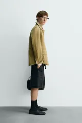 Cazadora de hombre de corte relajado, confeccionada en piel con acabado ante color mostaza/verde oliva. Presenta cuello solapa, manga larga con puño abotonado, cierre frontal de botonadura y cuatro bolsillos de plastrón visibles (uno en el pecho y tres en la parte inferior).