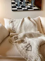 Manta de lana color crudo con bordados de flechas en color marrón.