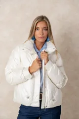 Campera puffer de acabado satinado en color beige, con cuello alto, cierre frontal y bolsillos laterales. Presenta un diseño moderno y sofisticado.