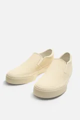 Zapatilla slip-on negra de tejido de algodón con elásticos laterales y suela color crema.