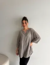 Blusa de viscosa gris con textura sutil, corte holgado y largo tipo túnica. Cuenta con cuello en V con pequeño tajo y un botón frontal visible, además de mangas tres cuartos anchas.