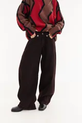 Pantalón de jean tipo balloon de tiro bajo, color marrón oscuro. Presenta un diseño con recortes curvos en las piernas, cierre frontal con doble botón en la cintura y costuras reforzadas.