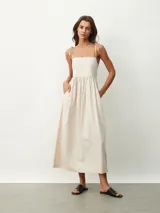Vestido midi color beige claro, de corte amplio y fluido, con tirantes finos ajustables mediante lazos en los hombros, escote recto y prácticos bolsillos laterales.