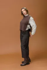Chaleco de punto color marrón, con cuello redondo y corte recto. Presenta un diseño minimalista con aberturas laterales amplias y detalle de tira con botón en los costados.