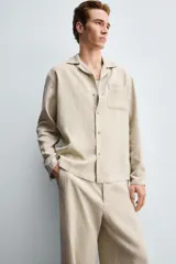 Camisa de corte relajado confeccionada en una mezcla de lyocell y lino. Presenta cuello bowling, manga larga con puño abotonado, bolsillo de plastrón en el pecho y cierre frontal con botones.