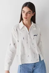 Camisa de manga larga color blanco con cuello polo y cierre frontal parcial. Presenta un estampado integral con motivos deportivos y un detalle bordado en el pecho.