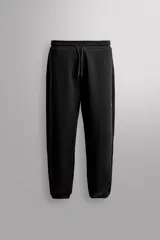 Pantalón jogger relaxed fit Zara Athleticz de tejido técnico compacto elástico con mezcla de algodón. Presenta cintura elástica ajustable con cordón, bolsillos laterales en la cadera, bolsillo trasero con cierre de cremallera, bajo ajustable con elástico y detalle de logo estampado en la pernera.