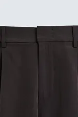 Bermuda negra de corte ancho (wide fit) confeccionada en tejido con mezcla de viscosa. Presenta pliegues en el delantero, bolsillos frontales y bolsillos de vivo en la parte trasera. Cierre frontal con cremallera y gancho metálico oculto.