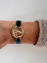 Pulsera dorada con dije redondo con la imagen de la Virgen de Fátima y cinta de terciopelo elástico color verde petróleo.