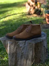 Botín tipo chukka de cuero color marrón, con cordones al tono y suela de goma oscura.