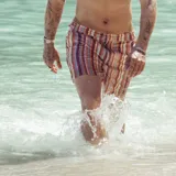 Short de baño con estampado geométrico en tonos tierra, naranja y violeta. Cuenta con pretina fija, hebillas metálicas laterales para ajuste, cierre frontal con botón a presión y tres bolsillos. Incluye interior con mesh hipoalergénico.