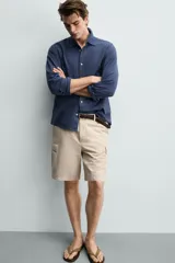 Bermuda cargo regular fit color beige, confeccionada en mezcla de algodón y lino con efecto lavado. Cuenta con bolsillos laterales tipo cargo con solapa en las perneras, bolsillos frontales, cierre frontal con cremallera y botón, y presillas para cinturón.