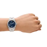 Reloj Emporio Armani plateado con caja de acero inoxidable de 41mm, esfera azul con patrón texturizado, agujas plateadas luminiscentes, indicador de fecha y pulsera de acero inoxidable con cierre desplegable.