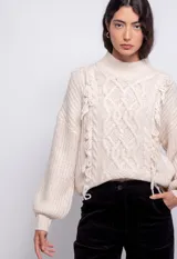 Sweater color crema de tejido trenzado con cuello alto, mangas largas abullonadas y detalle de flecos en el frente.