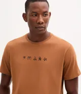 Remera de algodón color marrón claro, con cuello redondo y manga corta, de calce regular. Cuenta con un pequeño estampado frontal centrado con iconos alusivos a la playa.