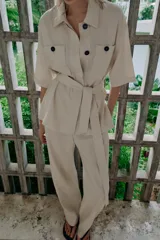 Chaqueta de estilo safari confeccionada en mezcla de lino, color azul marino, con cuello solapa, mangas cortas y cierre frontal con botones ocultos. Presenta bolsillos de parche en el pecho con solapa y botones, además de un cinturón ajustable del mismo tejido para anudar en la cintura.