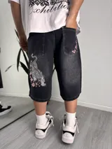Bermuda de denim negro con efecto acid wash, corte baggy y diseño largo hasta las rodillas. Cuenta con bolsillos traseros amplios y detalles bordados de un tigre y flores de cerezo (sakura) en la pierna y el bolsillo.