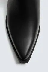 Bota corta negra estilo cowboy, con caña lisa, punta cuadrada y tirador trasero. Ajuste mediante cremallera lateral y tacón bajo.