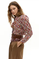 Camisa de popelina 100% algodón con estampado floral multicolor en tonos rojos, azules y amarillos sobre fondo blanco. Presenta cuello clásico camisero, hombros abullonados, mangas largas y botones de nácar en el frente.