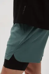 Short deportivo de doble capa color verde con calzas cortas negras incorporadas en el interior. Cuenta con tecnología DryMove™, cintura elástica negra con cordón ajustable, bolsillos laterales y aberturas en el bajo.