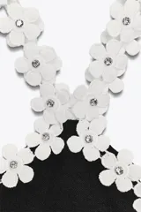 Body negro de tejido elástico con escote halter y detalle de flores blancas aplicadas en el contorno.