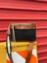 Bandolera de cuero color marrón y negro con correa regulable intercambiable con la palabra 'Rupia' en blanco y detalles de ojalillos.