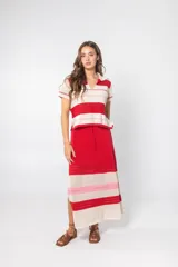 Falda midi de tejido de punto a rayas horizontales rojas y crudas, con una franja rosa. Tiene corte recto, cintura elastizada con cordón ajustable y abertura lateral.