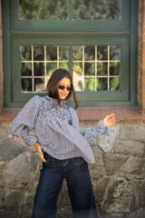 Blusa de algodón con estampado vichy en blanco y negro. Presenta un diseño con frunces en la parte superior del pecho, cuello alto con volado y mangas largas amplias con puños elásticos.