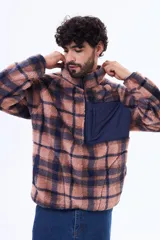 Campera de sherpa con diseño a cuadros en tonos marrón y azul marino. Presenta cuello alto, cierre frontal parcial y un bolsillo frontal con cierre en contraste de color azul marino.