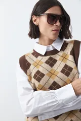 Chaleco tejido sin mangas con diseño de rombos tipo argyle en tonos marrón y beige, con cuello redondo y terminaciones acanaladas.