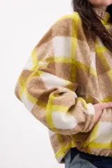 Campera bomber de paño italiano con diseño a cuadros en tonos beige, blanco y amarillo. Presenta un corte oversize, cuello alto, mangas murciélago y cierre frontal con botones a presión.