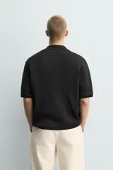 Camisa relaxed fit de punto tejida en hilatura con mezcla de algodón, color negro, con cuello solapa, manga corta y cierre frontal de botonadura.