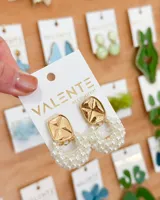 Par de aros colgantes con base cuadrada dorada y dije semicircular de perlas pequeñas.