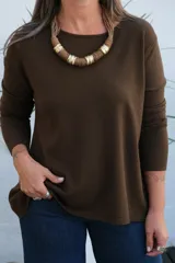 Sweater de punto color chocolate, con cuello redondo, manga larga y puños acanalados. Presenta un corte holgado con ruedo asimétrico.