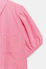 Camisa corta de cuello solapa y manga corta abullonada acabada en elástico, color verde con estampado de cuadros vichy. Cuenta con un bolsillo de plastrón en el delantero, bajo con elástico y cierre frontal con botones.