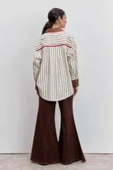 Camisa de corte oversize con estampado de rayas verticales, cuello clásico y cierre frontal de botones. Presenta dos bolsillos frontales en contraste con bordados de tréboles, además de puños y cuello en color sólido con detalles en amarillo.