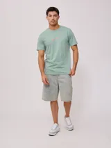 Remera negra de algodón con estampado en la espalda con palmeras, tabla de surf y texto en color blanco y fucsia.