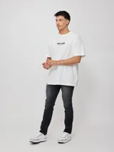 Remera de algodón blanca de corte oversize, con mangas cortas y cuello redondo. Presenta un gran estampado multicolor en la espalda con diseño gráfico de sol y texto, y un estampado más pequeño en el frente.