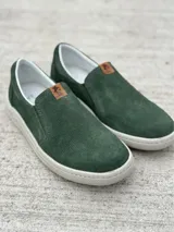 Zapato slip-on verde oscuro de gamuza con perforaciones, suela blanca y elástico lateral.