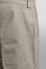 Pantalón de corte tapered fit color beige, confeccionado en tejido ligero de algodón con estructura rip stop. Cuenta con bolsillos de plastrón delanteros con acceso curvado, pinzas en las rodillas para mayor movilidad, y cierre frontal con cremallera y botón a presión.