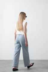 Pantalón de mujer de tiro medio, pierna amplia y recta, confeccionado en tela de algodón a rayas verticales finas celestes y blancas. Presenta bolsillos utilitarios grandes en la parte delantera.