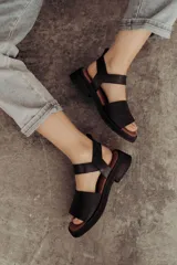 Sandalia de cuero color tostado con tiras anchas, tira en el talón y hebilla metálica rectangular ajustable. Cuenta con suela de goma con tacón bajo y plataforma.