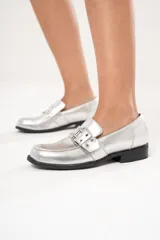 Mocasines plateados de cuero con hebilla y ojalillos.