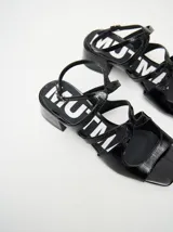 Sandalias de cuero con acabado charol color bordó, con punta cuadrada, tiras onduladas en el empeine y correa ajustable con hebilla en el tobillo. Cuentan con un taco bajo forrado.