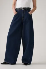 Jean de corte baggy y silueta barrel, confeccionado en denim rígido de color azul oscuro. Presenta costuras laterales curvadas que definen su forma característica, tiro alto y cierre frontal con botón y cremallera.