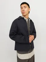 Campera aviadora negra de corte clásico, con cuello camisero, cierre frontal con cremallera, bolsillos laterales y puños ajustados. Confeccionada en tejido plano de poliéster y algodón.