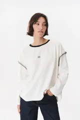 Remera de manga larga con corte oversized, color azul marino con cuello redondo en contraste color marrón. Presenta costuras decorativas a contratono hechas a mano en la zona de los hombros y logo bordado en el centro del pecho.