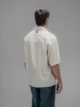 Camisa de manga corta color blanco roto, con cuello clásico y cierre frontal de botones.