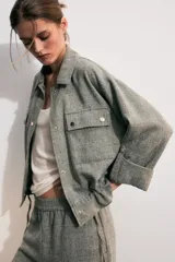 Chaqueta corta gris de tejido texturizado con cuello solapa, manga larga con trabilla, bolsillos delanteros con solapa y cierre frontal de botones metálicos.