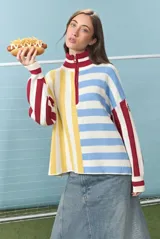 Sweater de punto de algodón con diseño de bloques de rayas verticales y horizontales en colores rojo, amarillo, azul y blanco. Presenta cuello alto con cierre frontal parcial y mangas largas con puños acanalados.